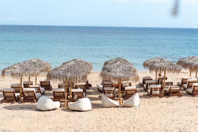Ξαπλώστρες και ψάθινες ομπρέλες στην παραλία με θέα στο Αιγαίο