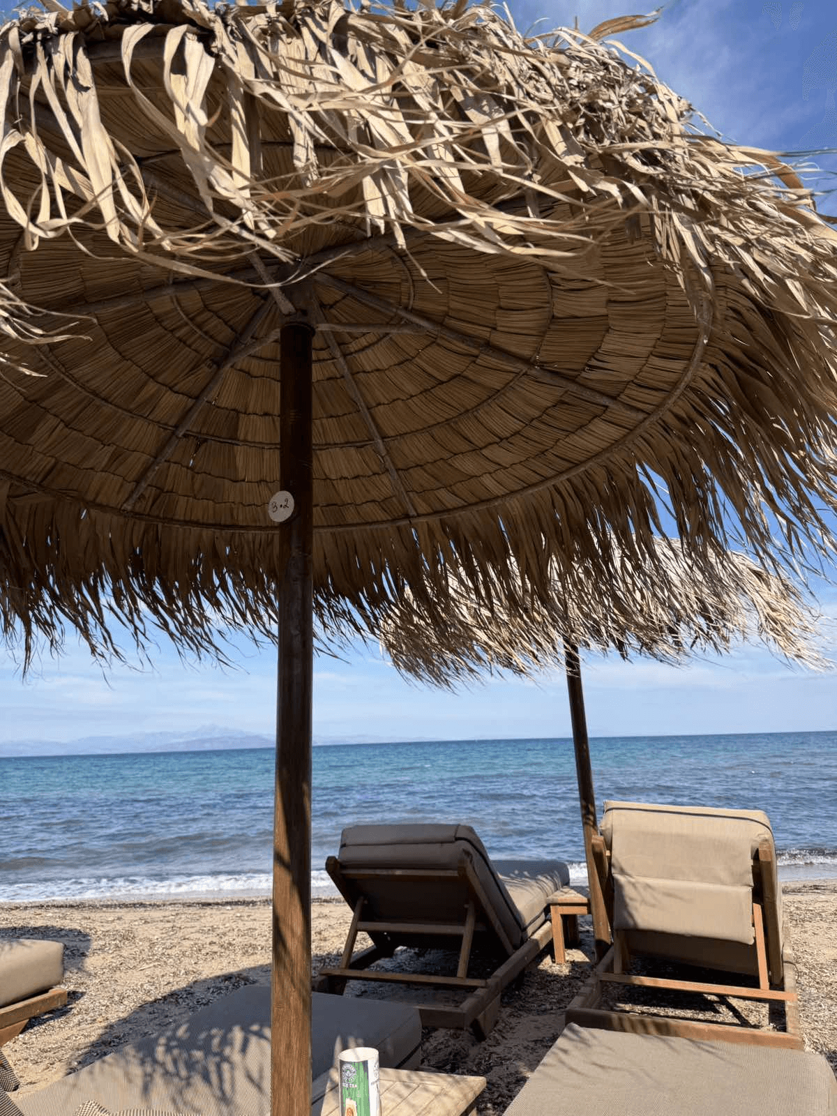 Ξαπλώστρα κάτω από ψάθινη ομπρέλα με θέα στη θάλασσα